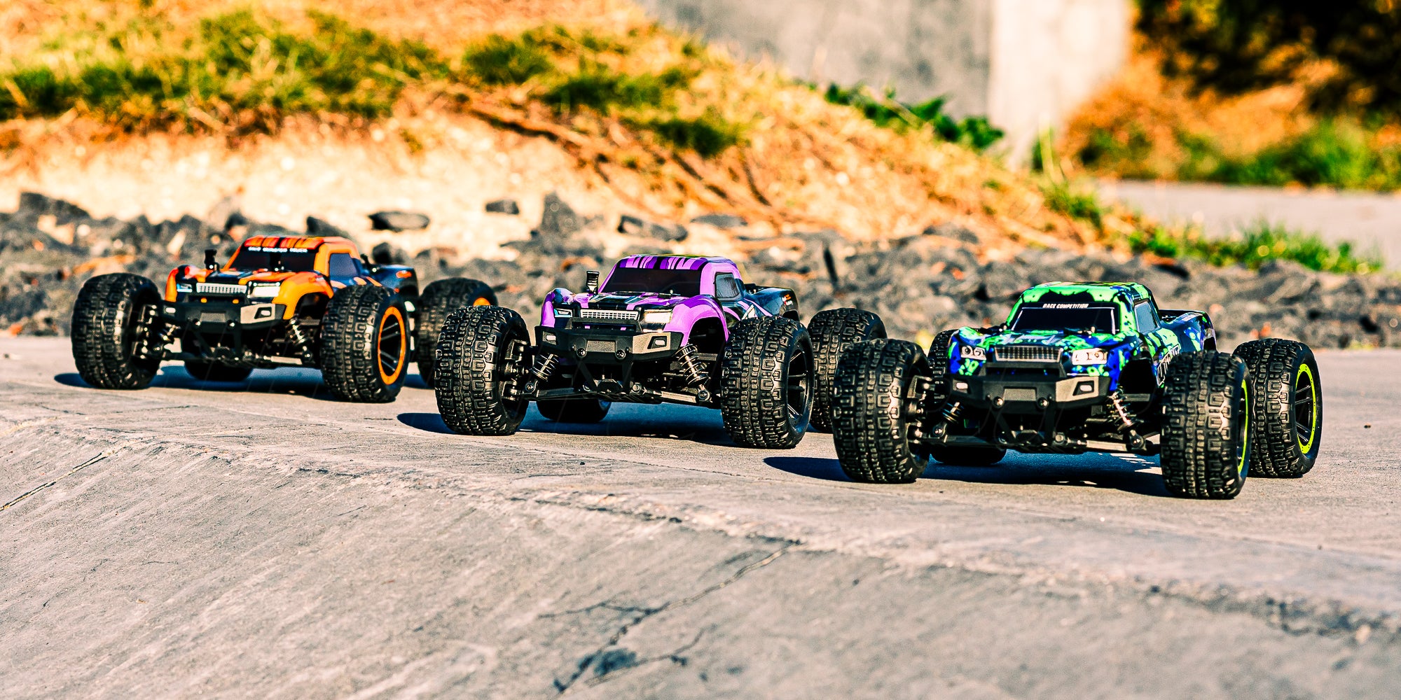 Tre farverige Hunter MT10 fjernstyrede monster trucks vist sammen i et bakket udendørs terræn.
