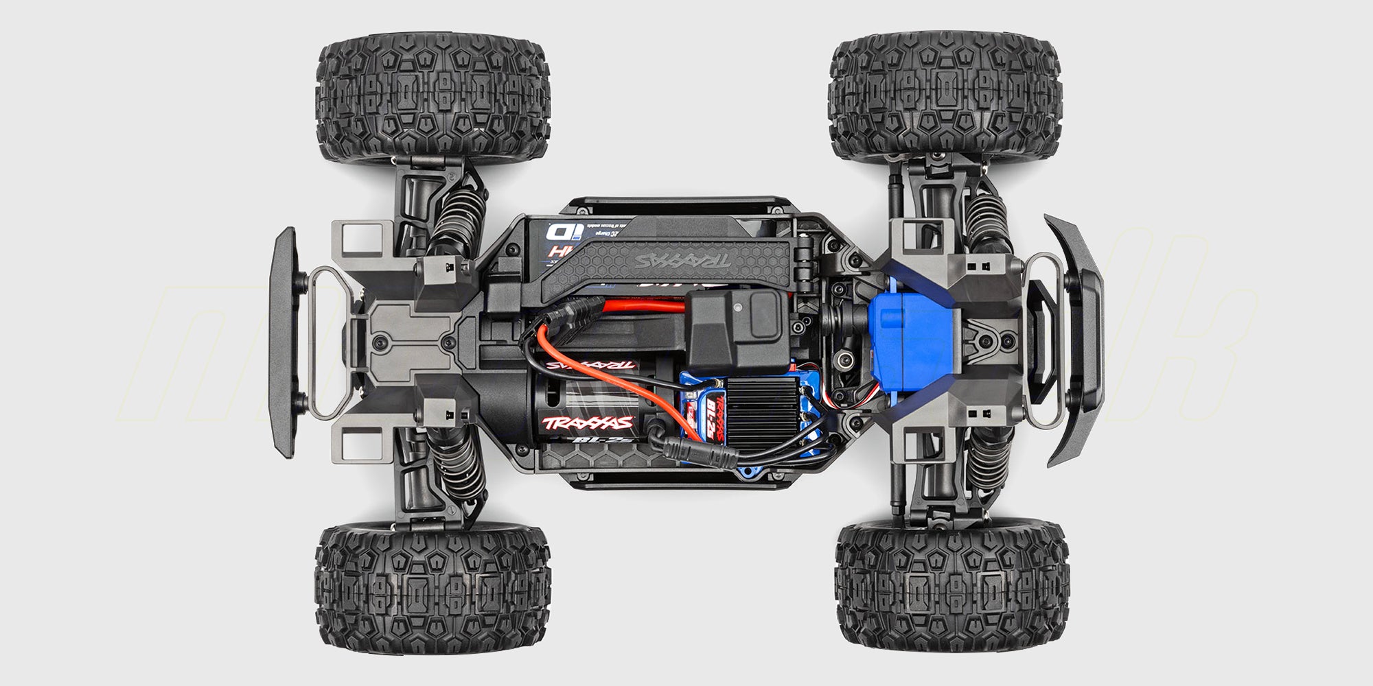 Blå og orange Traxxas Mini Maxx fjernstyret monster truck i et vildt hop over grus og sten.