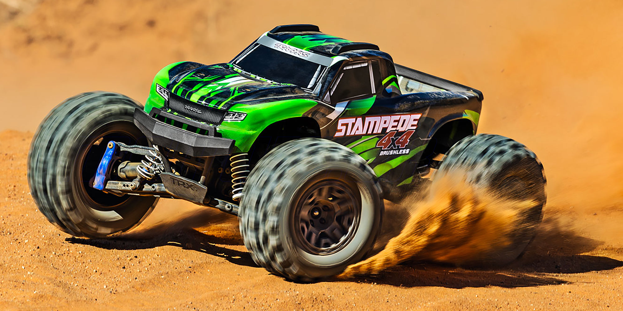 Blå Traxxas Stampede 4x4 BL-2S monster truck kører gennem vandpytter og sprøjter med mudder i terrænet.