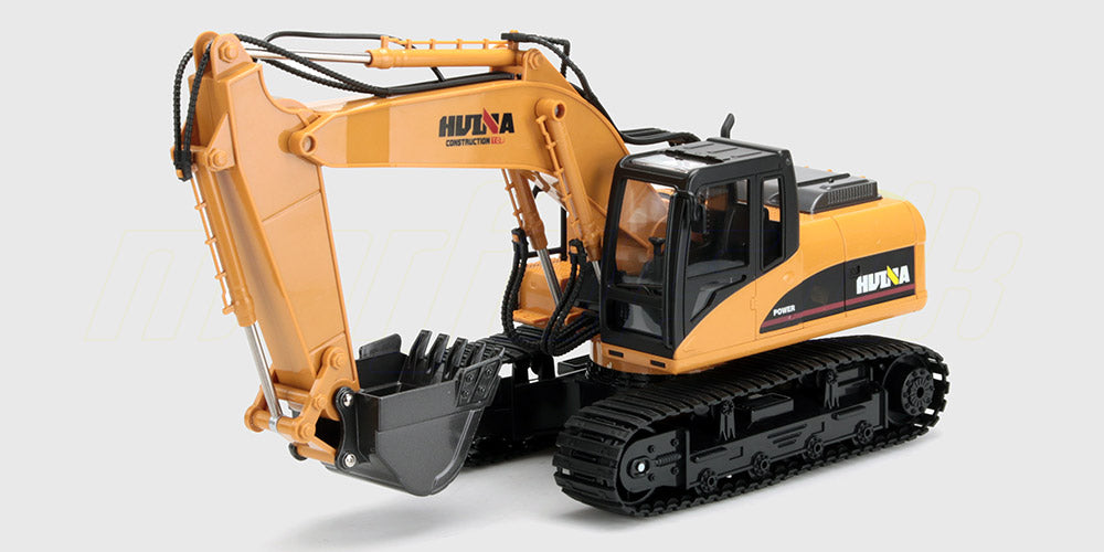 Gul fjernstyret gravemaskine med bevægelig skovl og larvefødder vist på hvid baggrund.