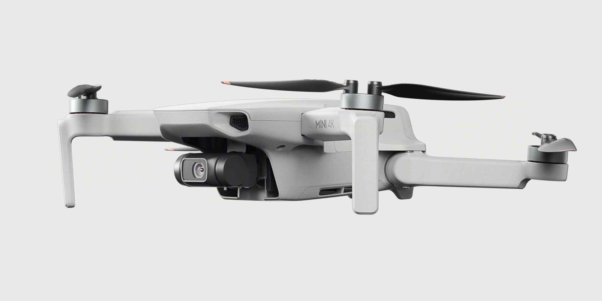 Grå DJI Mini 4K drone i luften over en kyststrækning med blåt vand og grønne klipper.