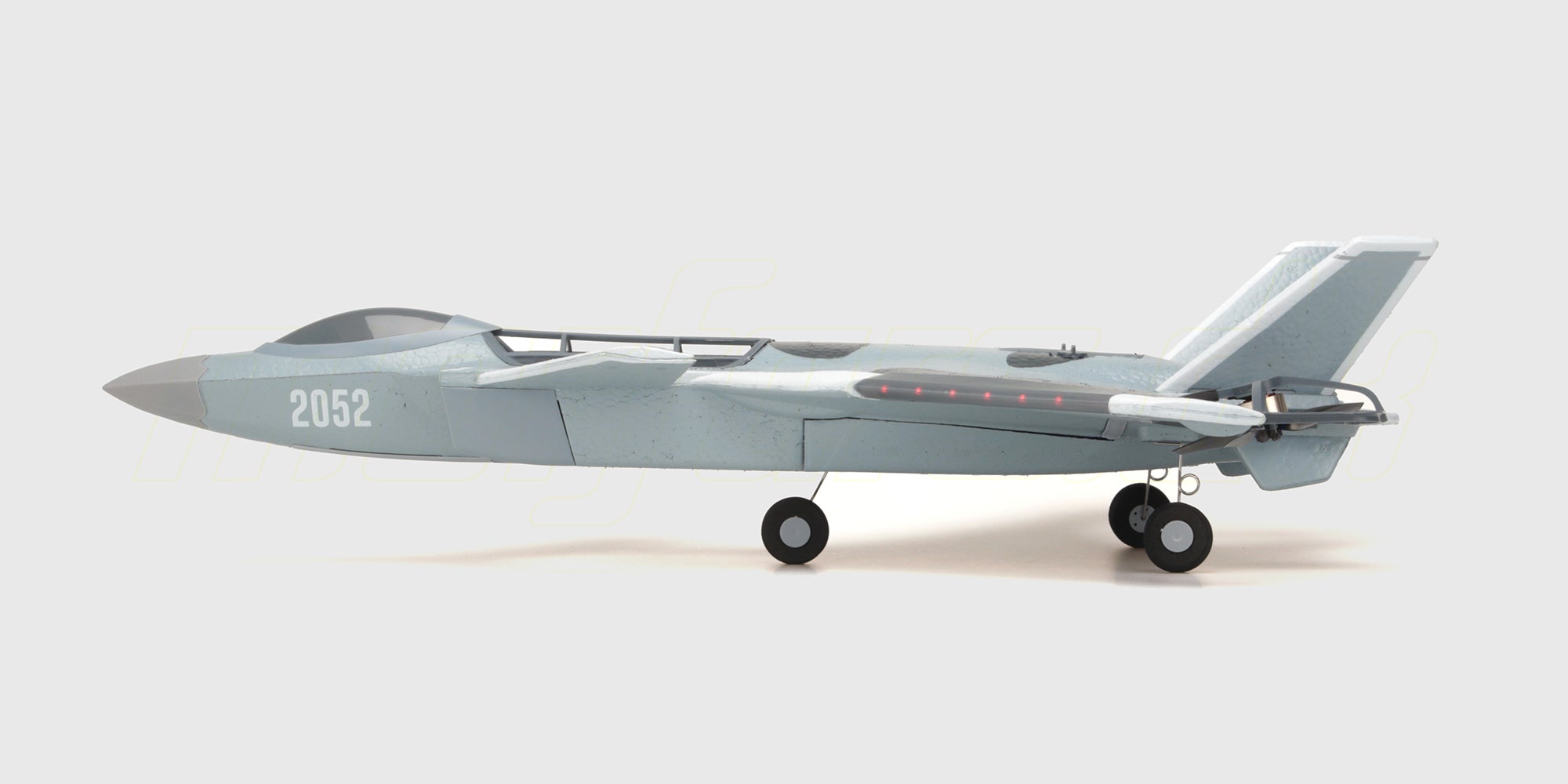 Gråt Fighter Jet Brushless fjernstyret fly med camo-mønster og rød næse klar til start på en græsmark.