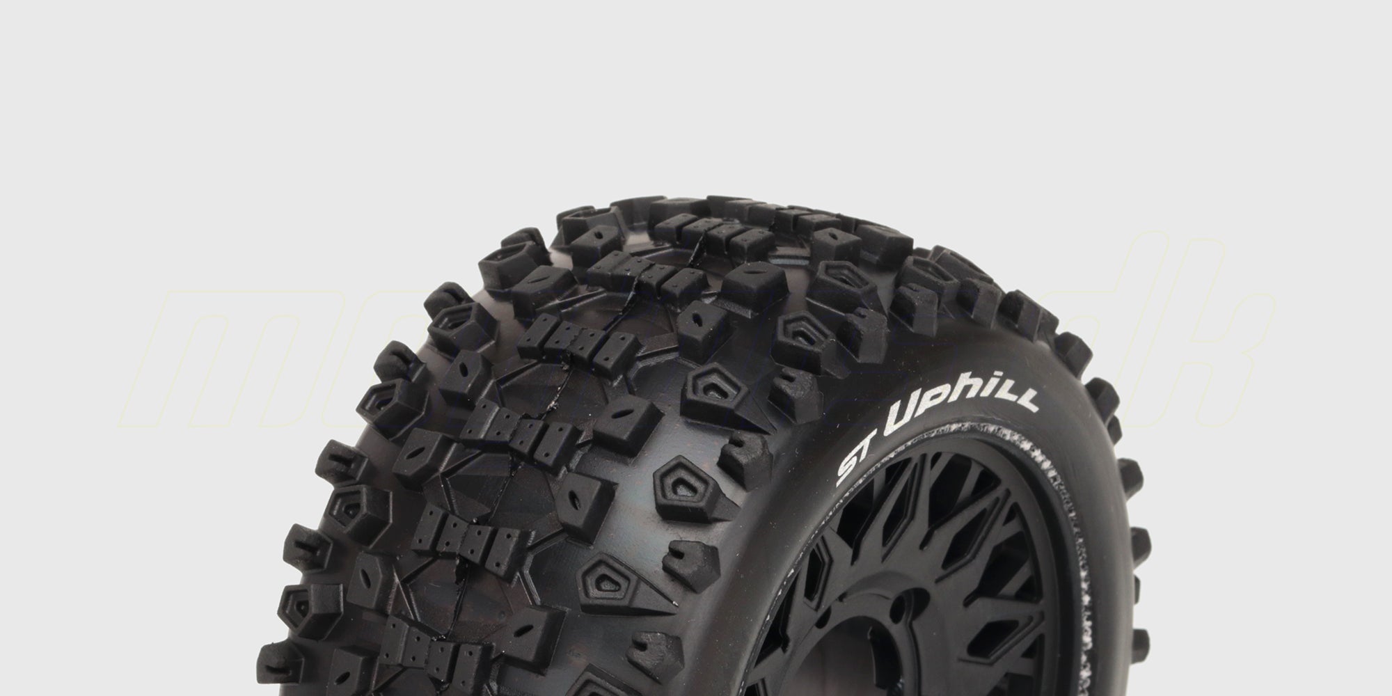 To sorte ST-Uphill dæk med groft dækmønster monteret på hvide fælge til fjernstyrede biler.