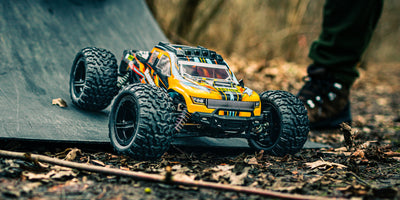 Blå Tornado Brushless fjernstyret monster truck kører hurtigt gennem svinget på en grusvej og hvirvler støv op.