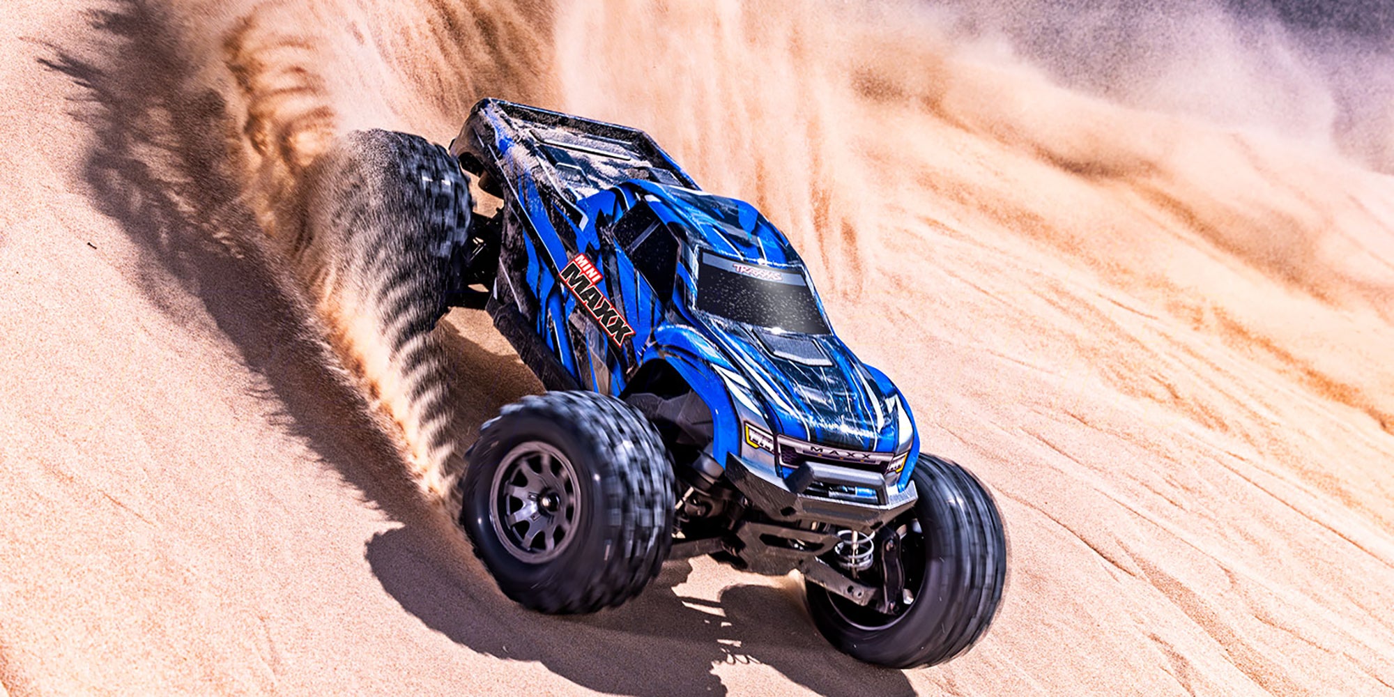 Traxxas Mini Maxx monster truck i orange med store offroad-hjul og kraftig undervogn på hvid baggrund.