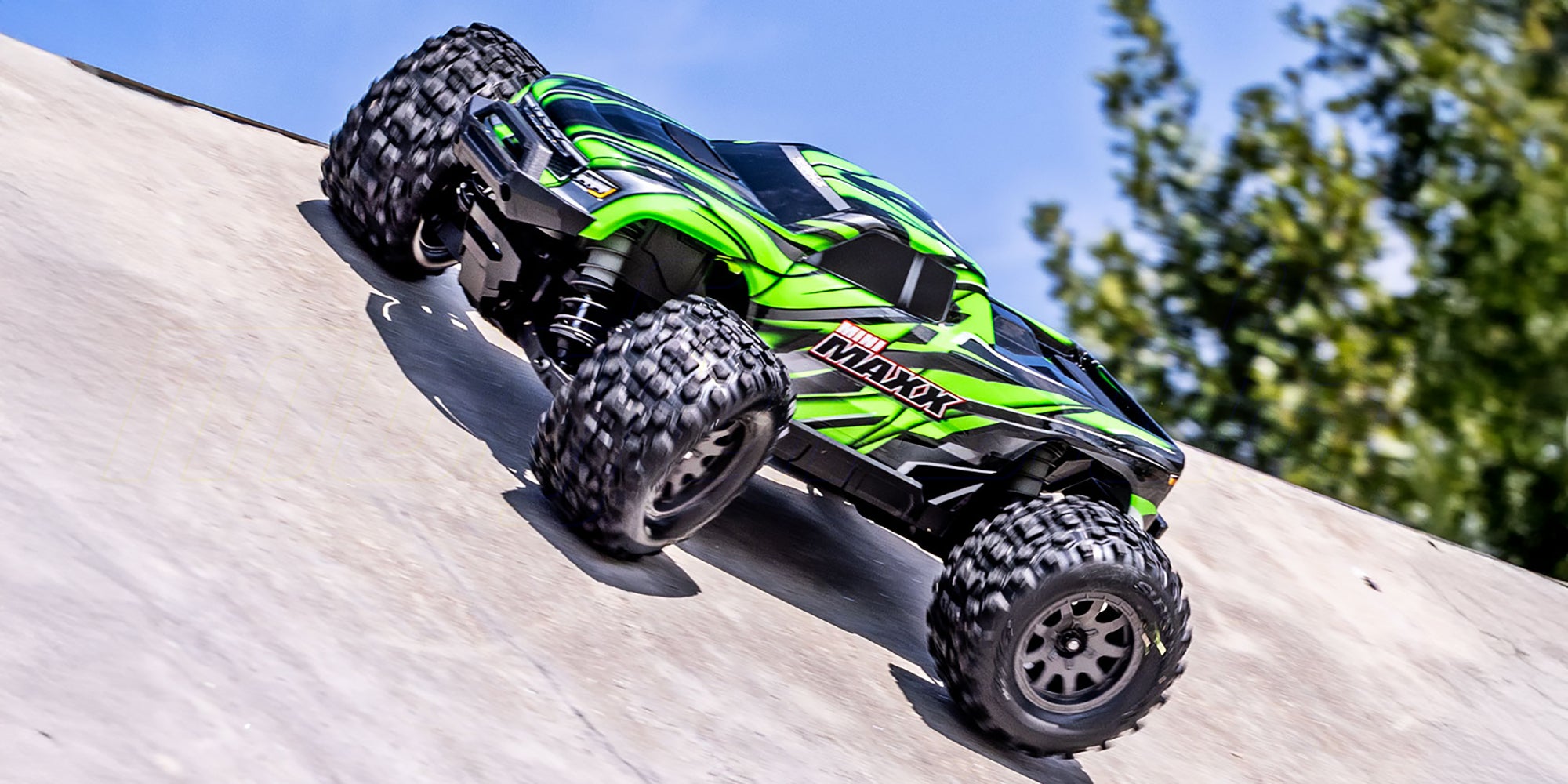 Sort Traxxas Mini Maxx monster truck med blå detaljer kører hurtigt gennem mudret terræn.