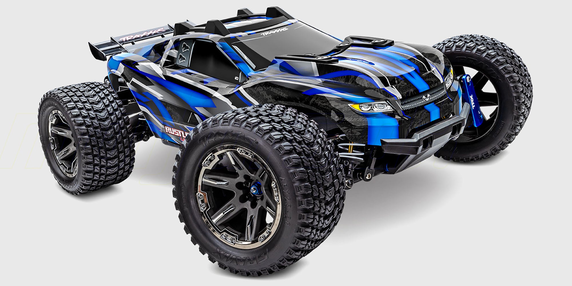 Blå Traxxas Rustler 4x4 Ultimate fjernstyret bil med store offroad dæk set skråt forfra på hvid baggrund.