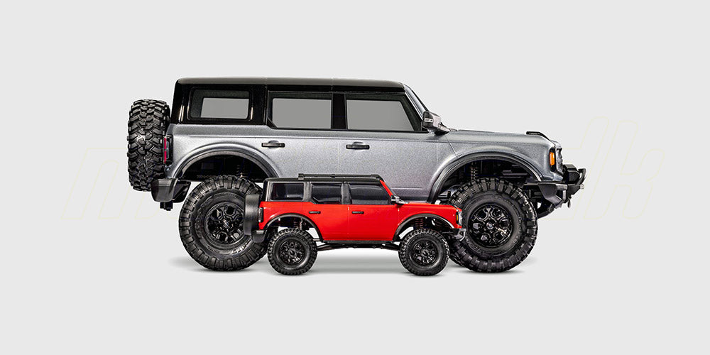 Størrelsessammenligning af en rød TRX-4M Ford Bronco i 1:18 og en større 1:10 RC crawler på hvid baggrund.